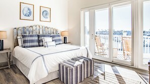 Un dormitorio con una cama grande, un banco y vistas de la ciudad a través de amplias ventanas.