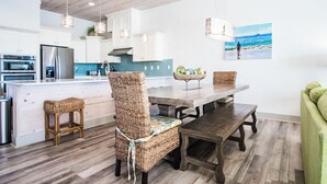 Una cocina moderna con armarios blancos, un refrigerador de acero inoxidable y una mesa de comedor de madera con sillas de mimbre.