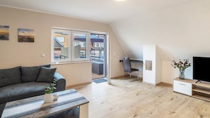 Ein modernes Wohnzimmer mit einer Couch, einem Couchtisch, einer TV-Konsole und Blick durch eine Glastür auf einen Balkon.