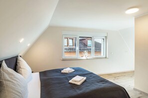 Une chambre à coucher avec un lit, des oreillers, une fenêtre et une vue sur un bâtiment à l’extérieur.