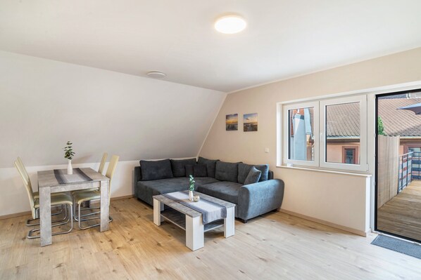 Un salon moderne avec un canapé gris, une table à manger et des chaises, ainsi qu’une petite table basse.