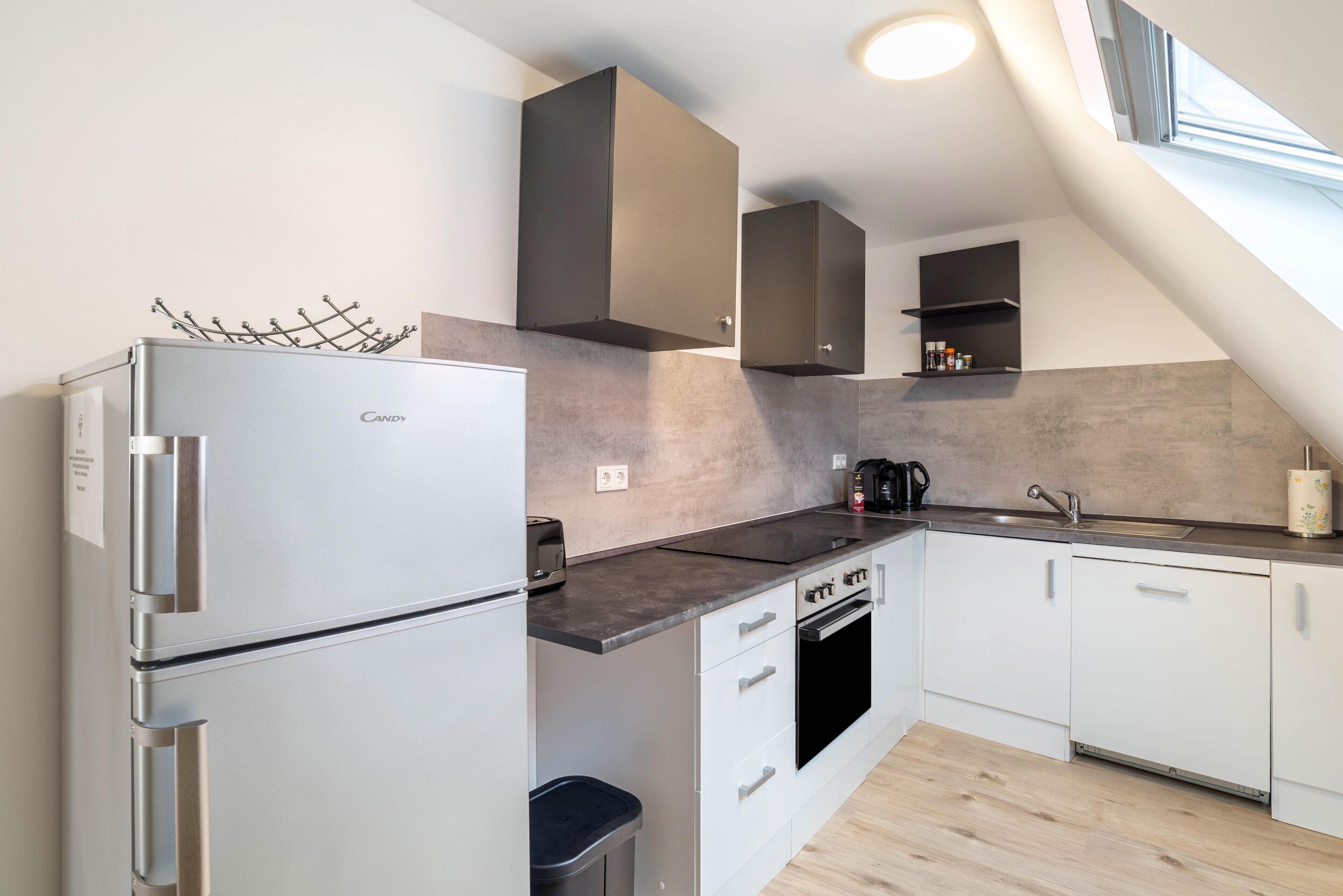 Eine moderne Küche mit integriertem Kühlschrank, Backofen und Spüle, mit Betonrückwand und Holzboden.