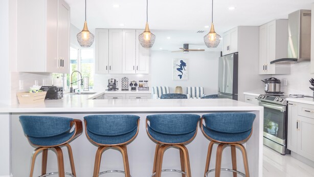 Una cucina moderna con mobili bianchi, una grande isola con sgabelli da bar, elettrodomestici in acciaio inossidabile e illuminazione a sospensione.