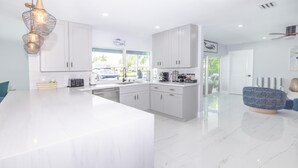 Una cucina moderna con mobili bianchi, un'isola grande e un'area pranzo con una sedia blu.