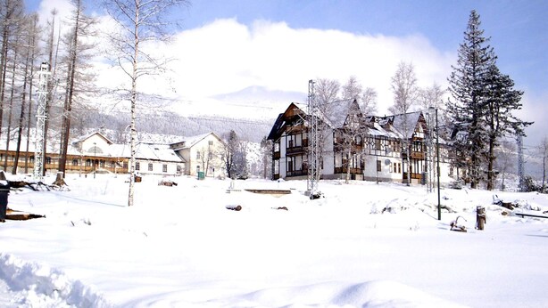 En snøklædt landsby med traditionelle træhuse, en klar himmel og et bjerg i baggrunden.