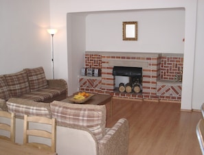 A living room with a brick fireplace, a plaid sofa, a wooden coffee table, and a small framed picture on the wall. - Modern, spacious, well equipped apartment in High Tatras mountains (Vysoké Tatry)