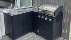 An outdoor kitchen with a grill, sink, and cabinets, set on a wooden deck.