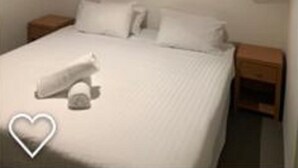 A hotel room with a large bed, two bedside tables, a wall-mounted light fixture, and a window with blinds.