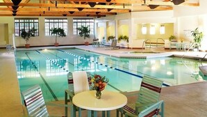 En indendørs swimmingpool med træloft, omgivet af liggestole og et bord med blomster.
