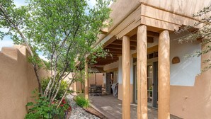 A covered patio area with wooden columns, a stone pathway, and lush greenery. - Quail Run 640 | Kiva Fireplace | Private Patio | 2-Car Garage | Golf Course | Pool & Hot Tub (Santa Fe)