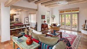 A spacious living room with a high ceiling, wooden beams, a large window, and a cozy seating area with a sofa and armchairs. - Quail Run 640 | Kiva Fireplace | Private Patio | 2-Car Garage | Golf Course | Pool & Hot Tub (Santa Fe)