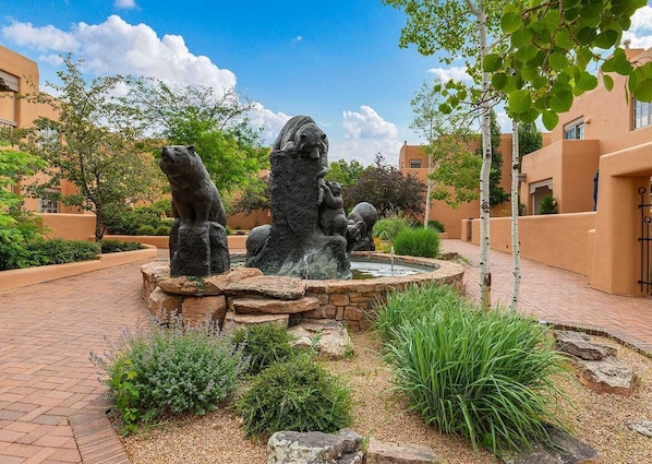 A courtyard with a stone fountain, surrounded by greenery and buildings with a consistent architectural style.