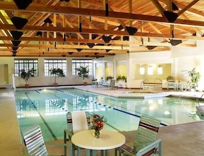 An indoor swimming pool with a wooden ceiling, clear pool water, and lounge chairs.