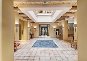 A hotel lobby with a tiled floor, a central blue rug, wooden ceiling beams, and a skylight.