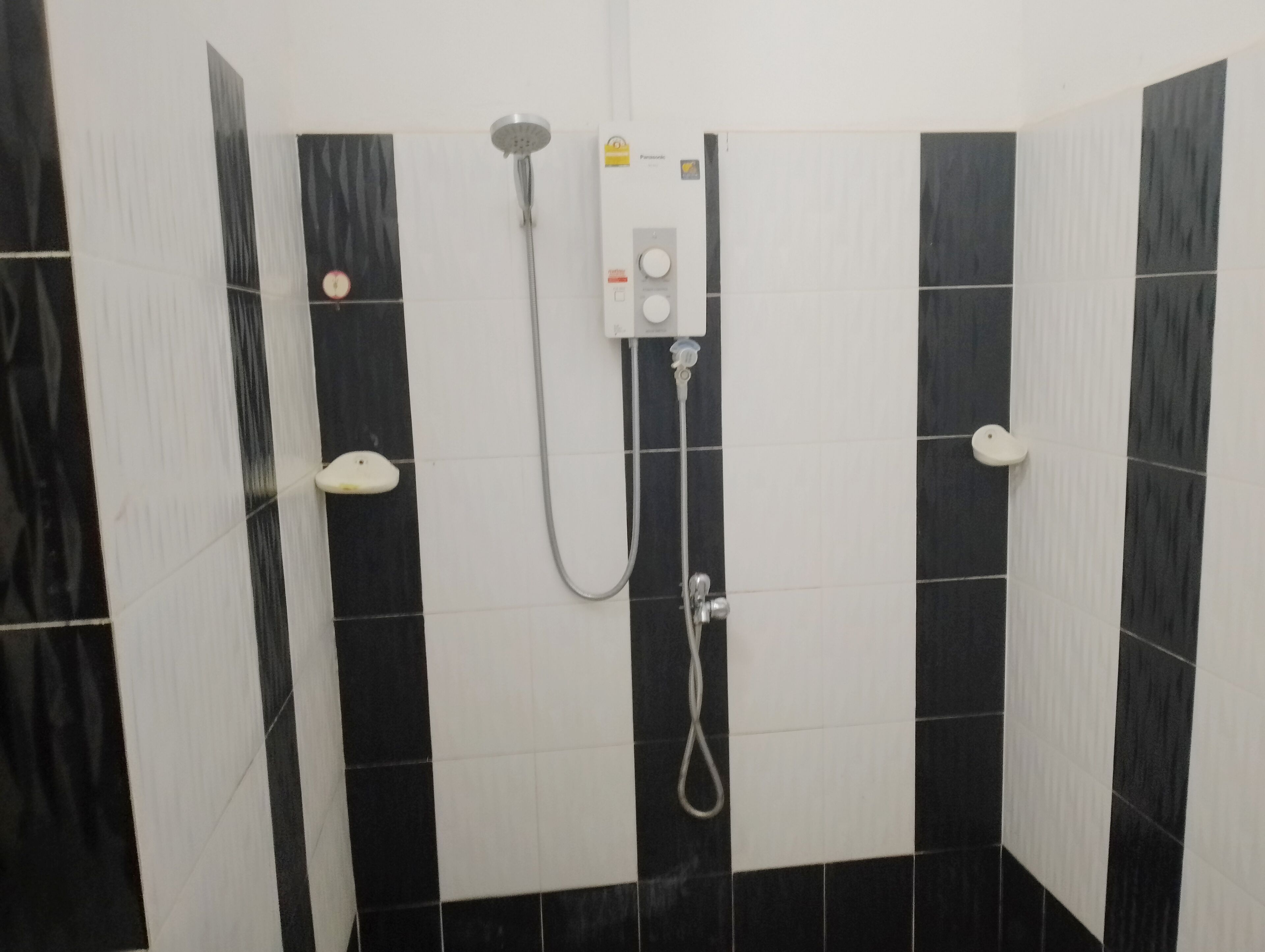 Casa de banho com azulejos a preto e branco, chuveiro com chuveiro manual e painel de controlo fixado na parede.