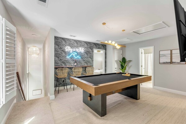 A modern room with a pool table, a neon sign, and a stone wall.