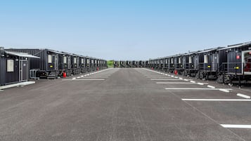 Une rangée de petits bâtiments modulaires noirs identiques, avec des marquages blancs sur le sol, disposés en ligne droite.