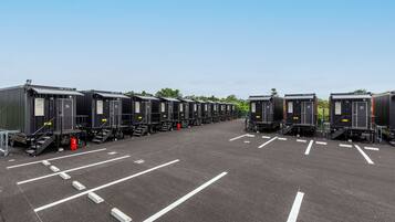 A row of portable cabins with numbered doors, arranged in a parking lot with marked parking spaces.