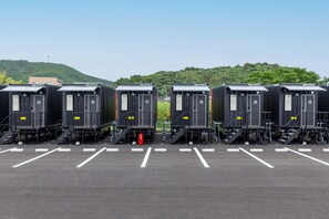 Eine Reihe von mobilen Toiletten auf einem Parkplatz, im Hintergrund ein grüner Hügel.