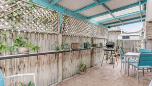 Un patio couvert, agrémenté d’une clôture en bois, de plantes en pot, d’un barbecue et de mobilier d’extérieur.