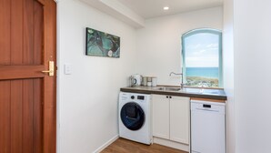 A compact kitchen with a washing machine, dishwasher, and a view of the sea through a window.