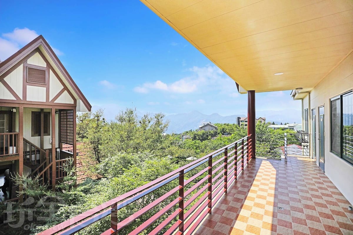 A balcony with a checkered floor, a red railing, and a view of a mountainous landscape.