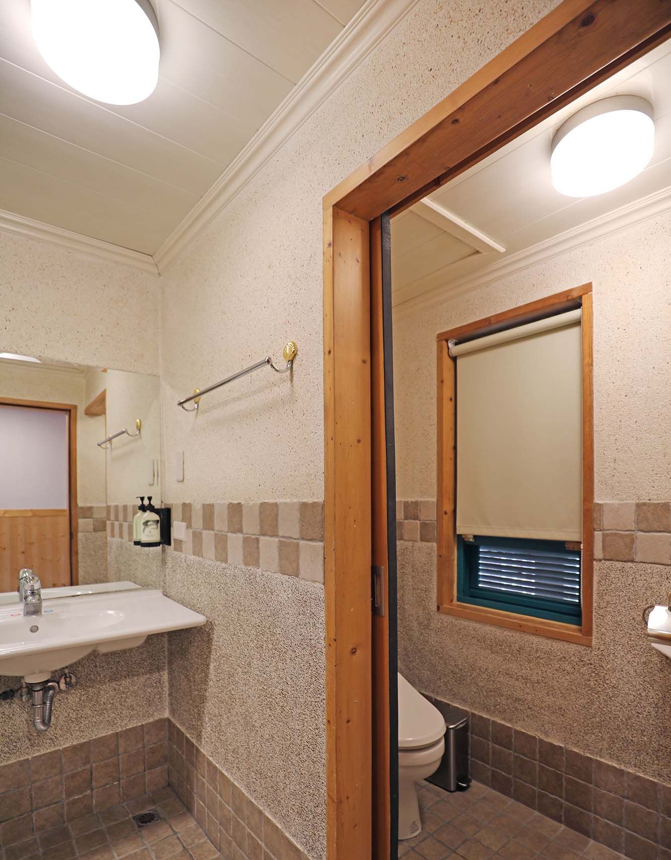 A bathroom with a sink, mirror, toilet, and a window with blinds.