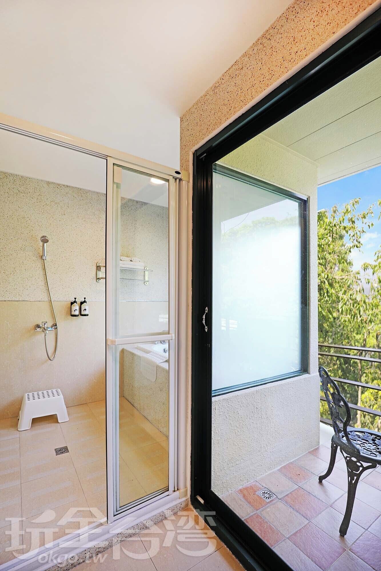 Un baño moderno con cabina de ducha de vidrio, un taburete y un balcón con una silla.