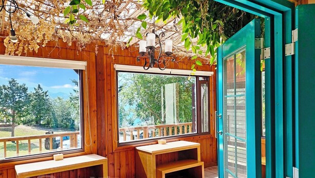 A wooden cabin with large windows, a bench, and a teal door. - Baili Manor Cing Jing (Ren'ai)