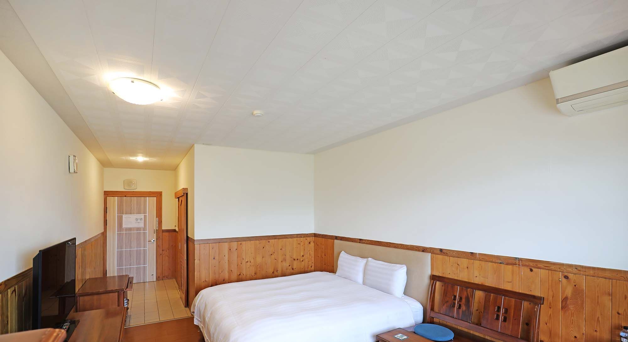 Habitación de hotel con cabecera de madera, cama con ropa blanca, escritorio de madera, una silla y un televisor.