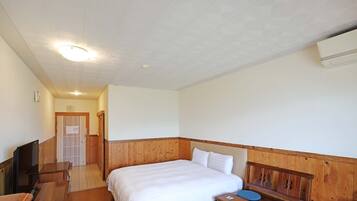 Habitación de hotel con cabecera de madera, cama con ropa blanca, escritorio de madera, una silla y un televisor.