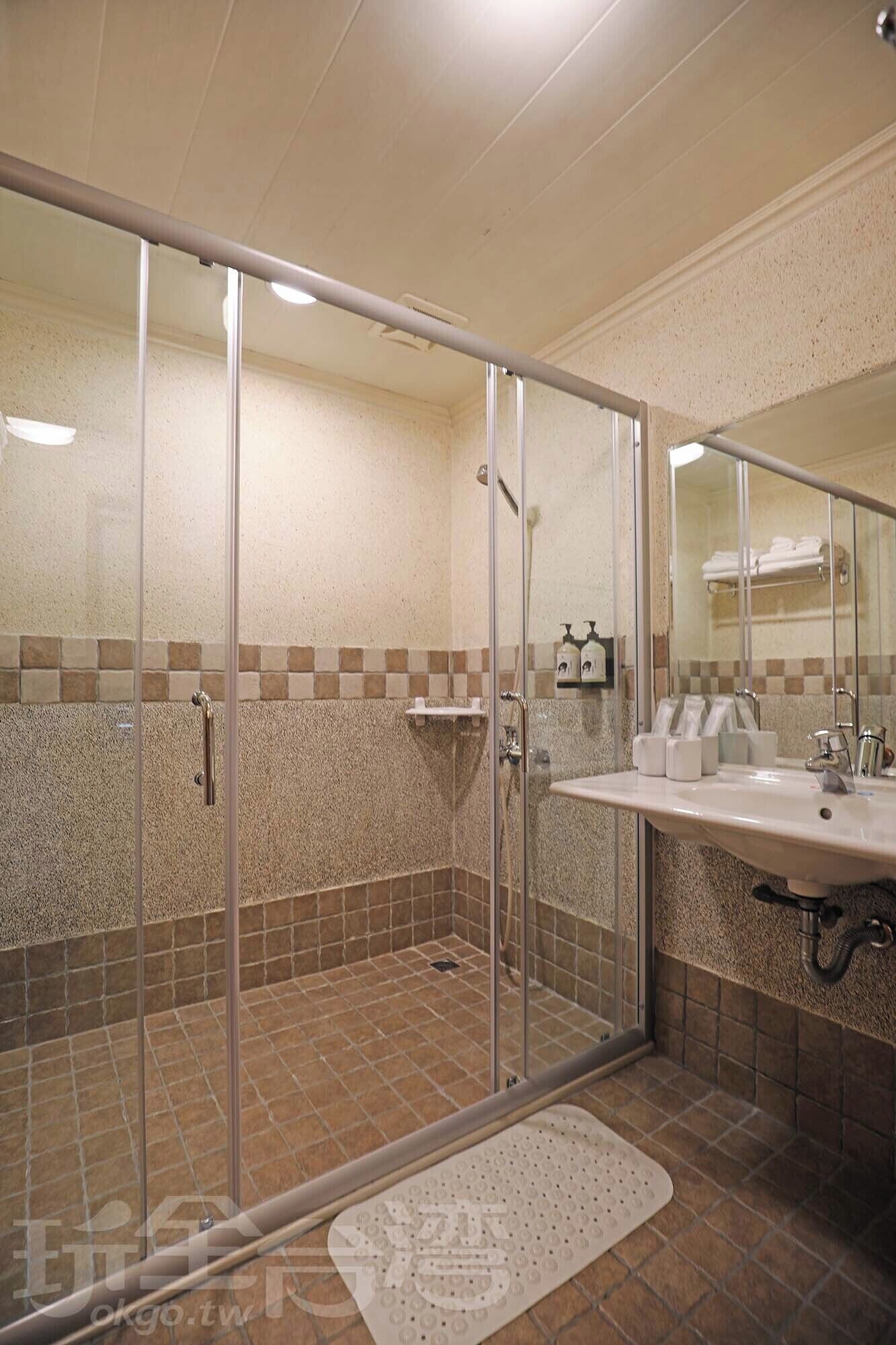 Een douche met glazen deuren, een wastafel met spiegel en een betegelde vloer.