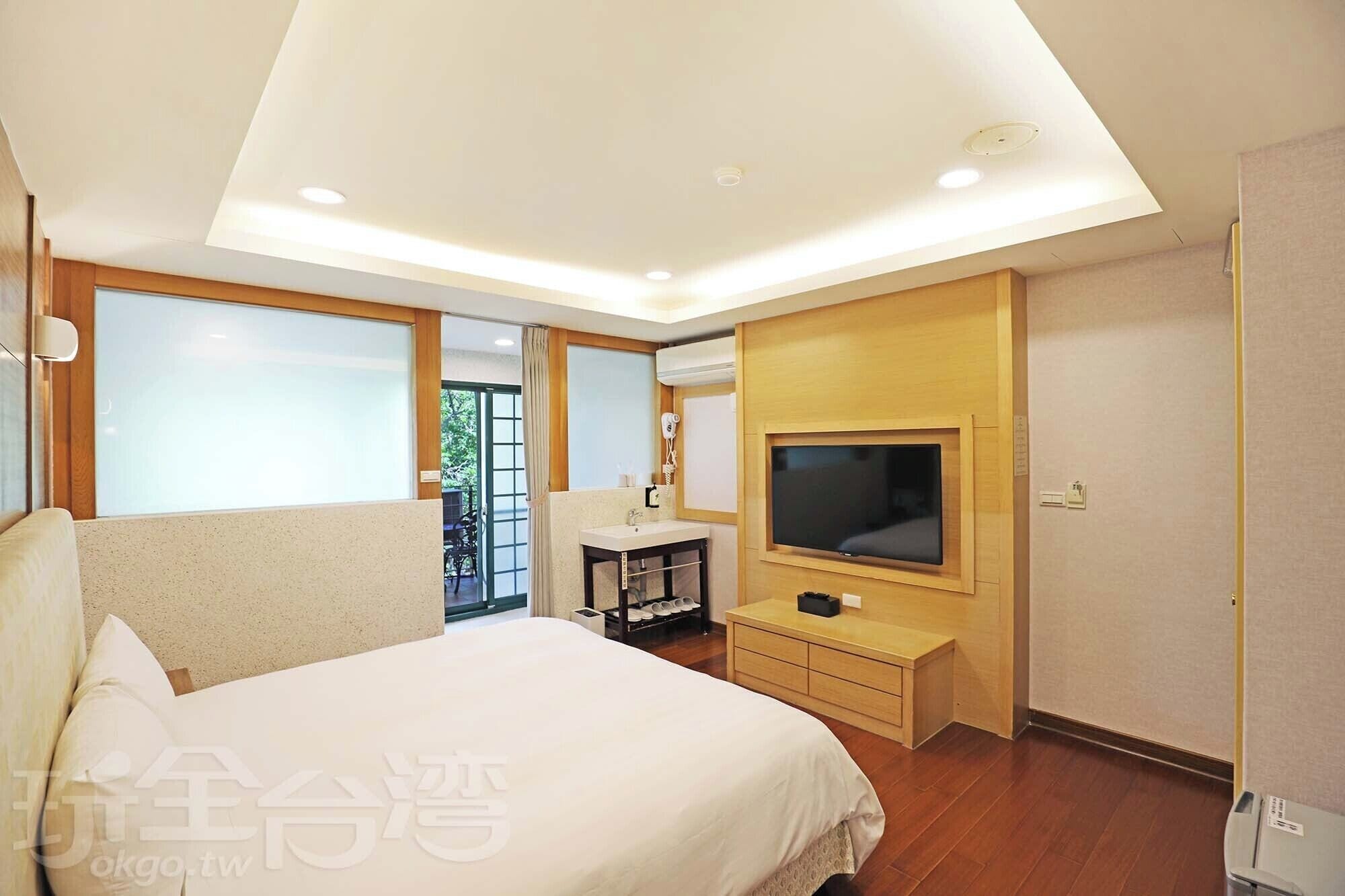 A modern hotel room with a large bed, a TV, a desk, and a balcony with a view.