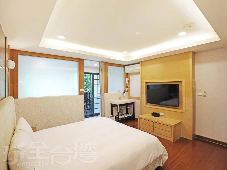 A modern hotel room with a large bed, a TV, a desk, and a balcony with a view.