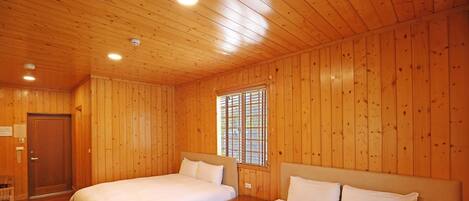 A wooden-paneled room with two beds, a window with bars, and a door.