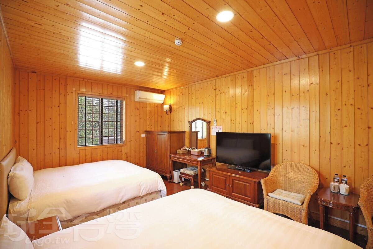 A wooden-paneled room with two beds, a television, a dresser, and a wicker chair.