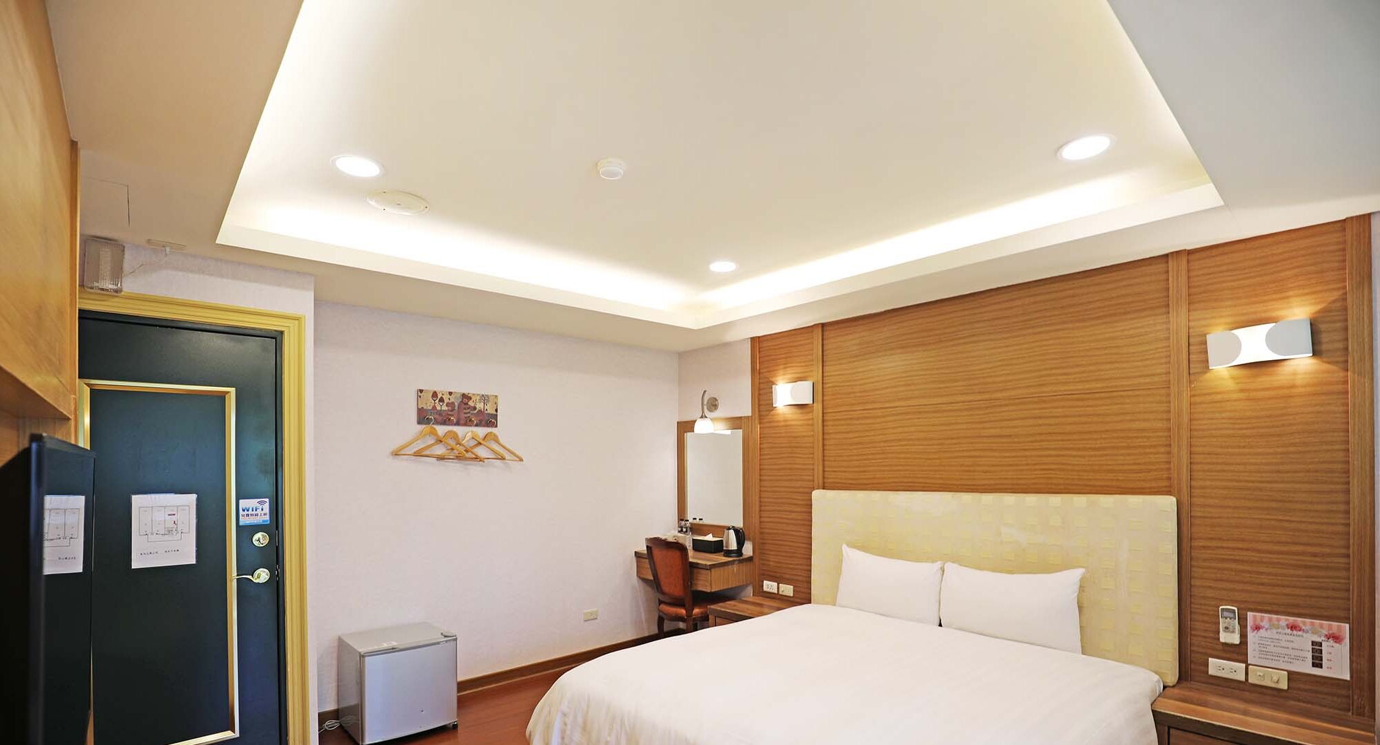 A hotel room with a bed, a desk, a chair, a mirror, and a wardrobe.