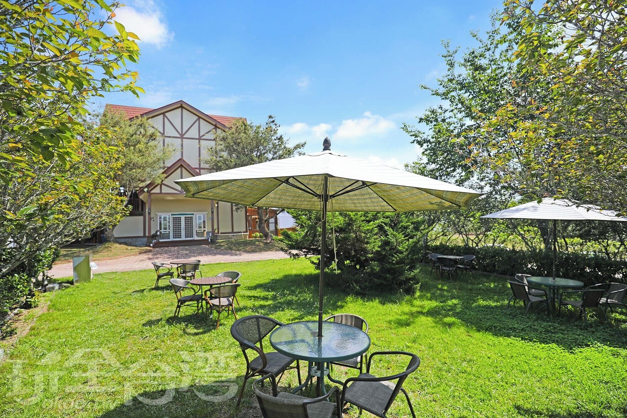 An outdoor patio with tables and chairs, a large umbrella, and a building in the background.