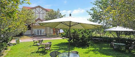 An outdoor patio with tables and chairs, a large umbrella, and a building in the background.
