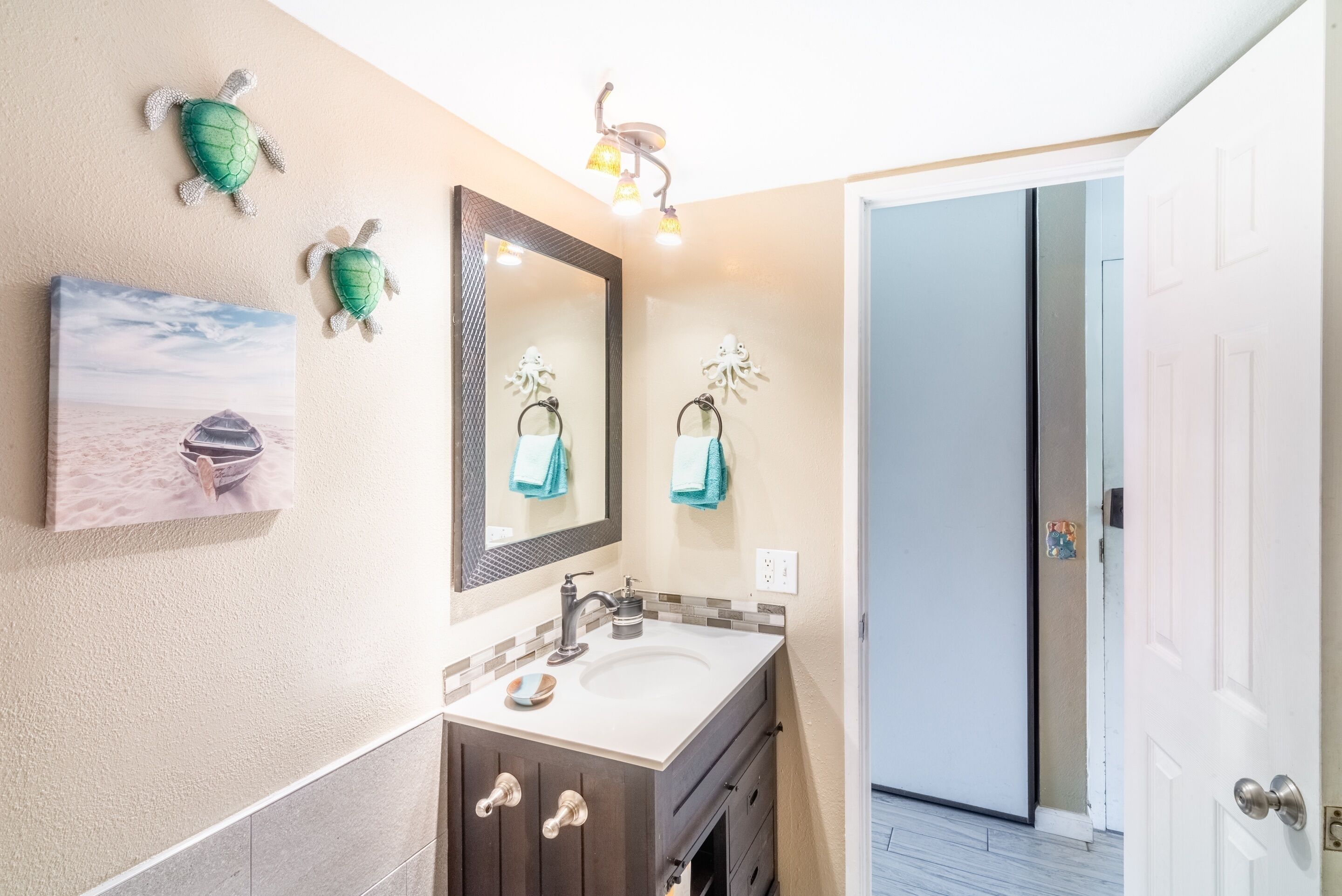 Een badkamer met een grote spiegel, een wastafel en decoratieve wanddecoratie van schildpadden.