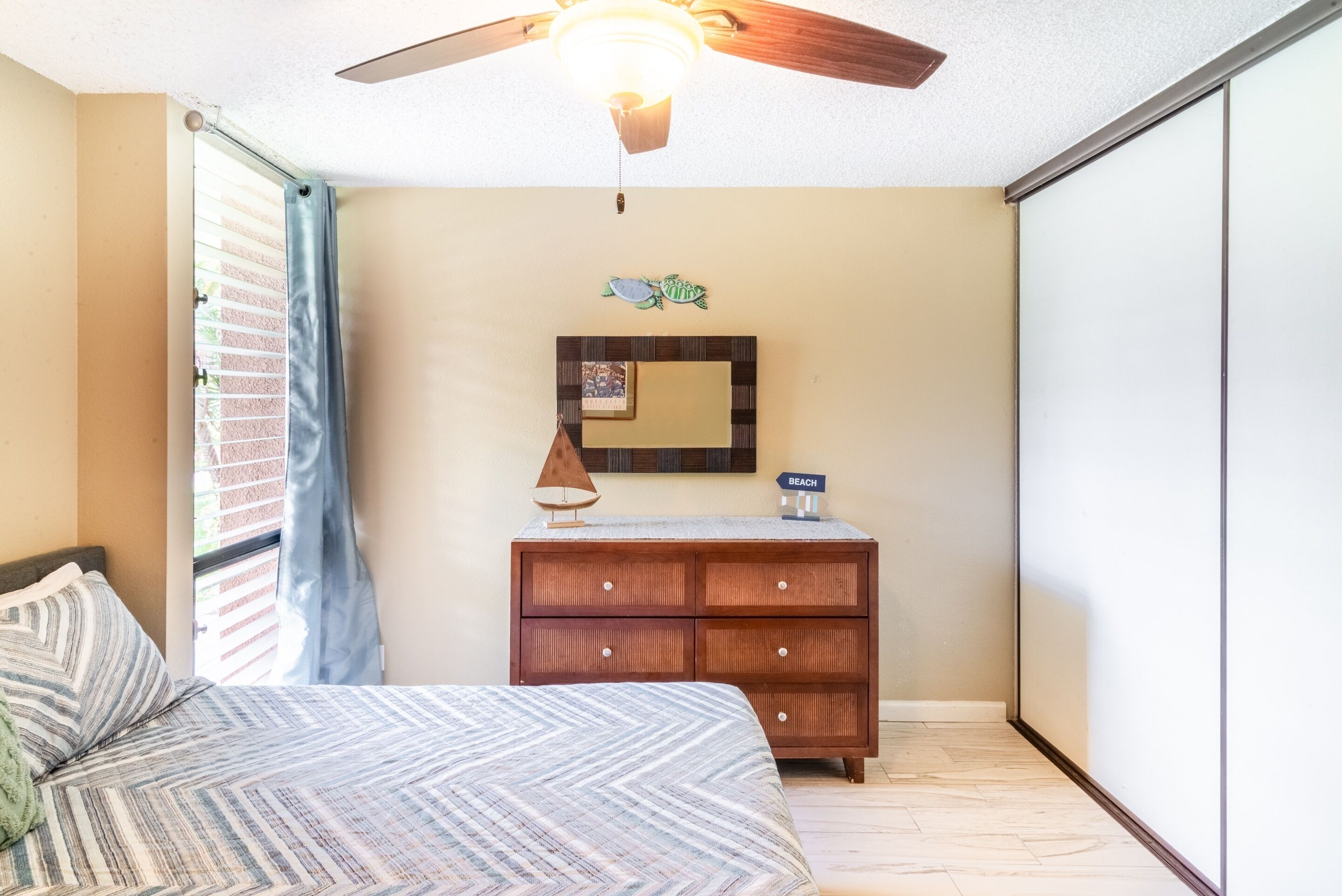 Een slaapkamer met een bed, een kaptafel, een plafondventilator en een spiegel aan de muur.