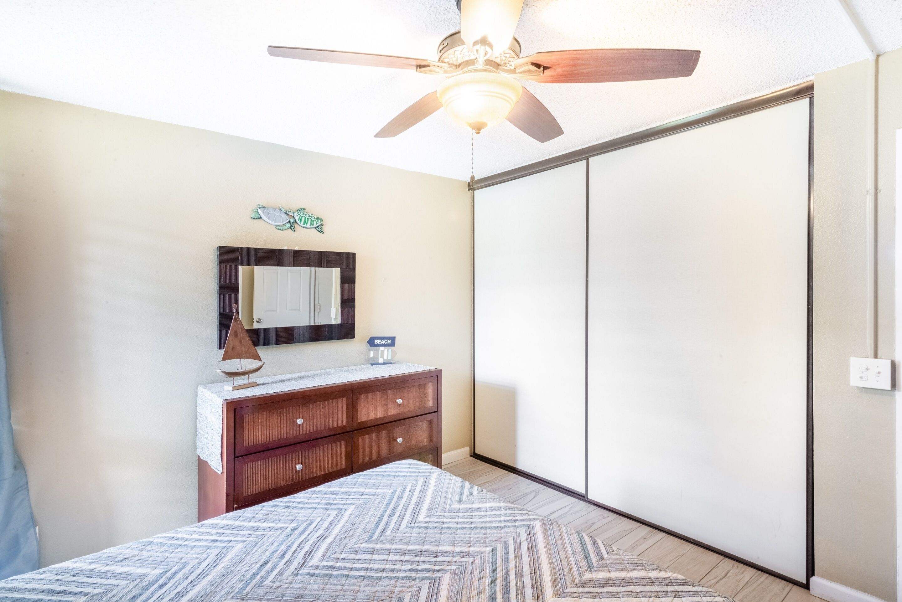 Une chambre à coucher comprenant un lit, une commode, un miroir et une porte de placard coulissante.