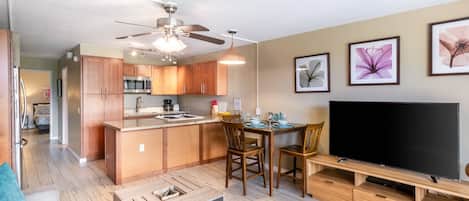 Un apartamento moderno con cocina, comedor y sala de estar. Cuenta con gabinetes de madera, ventilador de techo, televisión de pantalla plana y obras de arte en las paredes.