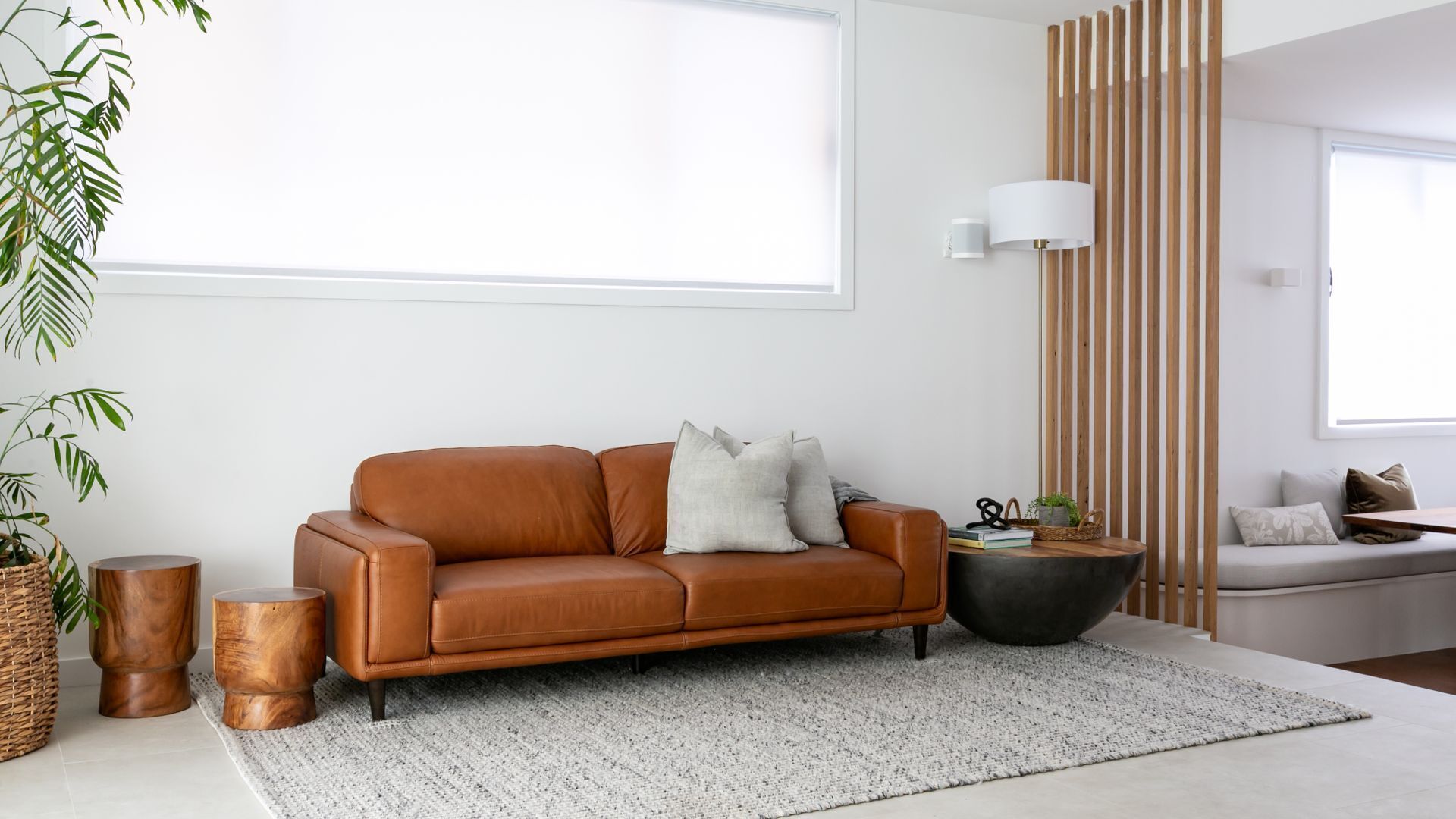 A modern living room with a brown leather sofa, a round coffee table, and a large window providing natural light.