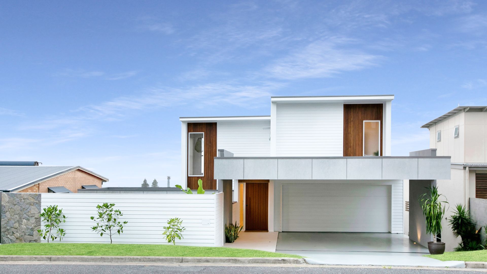 A modern two-story house with a garage, a stone wall, and small trees in the front yard.
