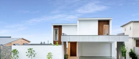 A modern two-story house with a garage, a stone wall, and small trees in the front yard.