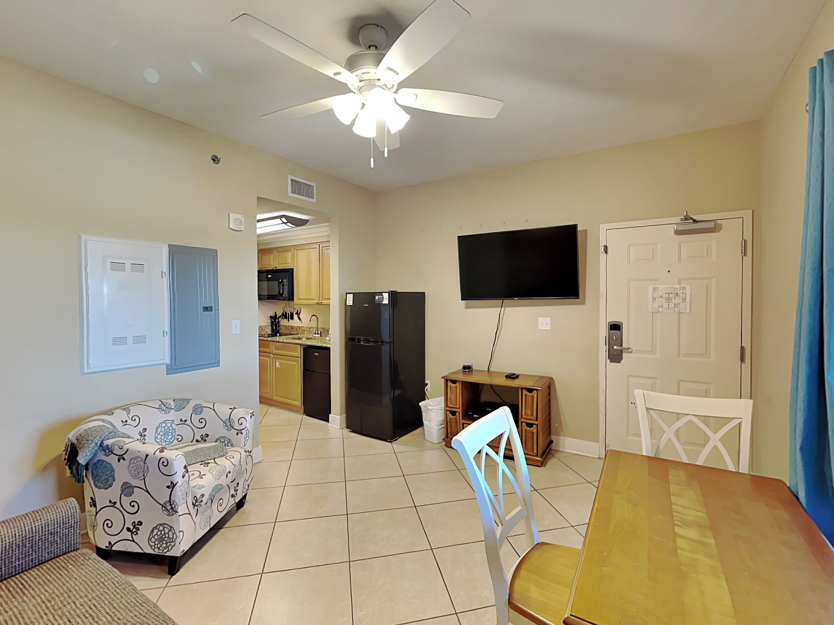 Un espacio habitable compacto con kitchenette, comedor, sofá y televisor fijado a la pared.