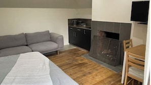 Un espace de vie compact comprenant un canapé, une table à manger avec des chaises, un coin cuisine avec des placards et une cheminée.