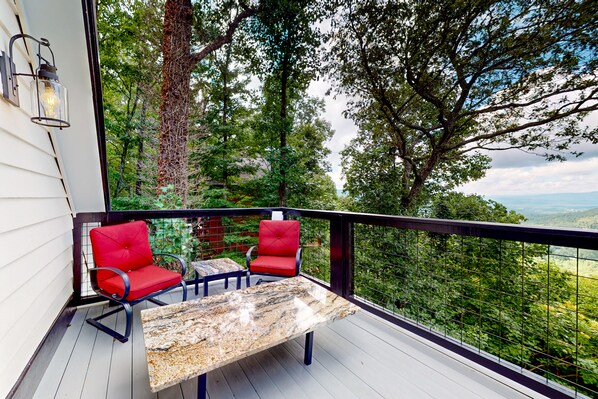 Relax on the balcony with two cushioned chairs and a table, taking in the serene views of the lush landscape.