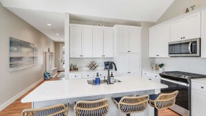 A modern kitchen with white cabinetry, a central island, bar stools, and a microwave. - Welcome to A View to A Chill | Navvy Town Duplex (Ottawa)